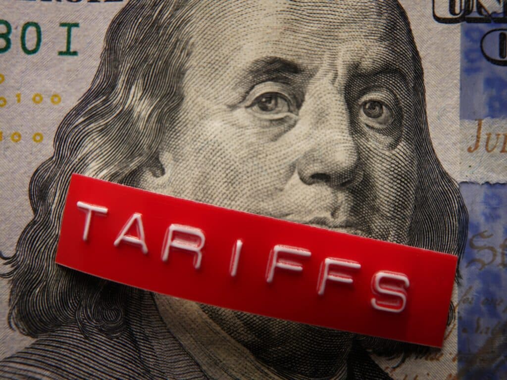 Red label with the word tariffs across a hundred dollar bill.