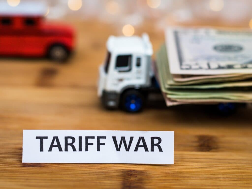 The words tariff war on a small paper sticker with a toy truck loaded down with money.